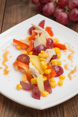 Salad with grapes and chicken on white dish. Wooden background. Top view