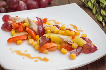 Salad with grapes and chicken on white dish. Wooden background. Top view