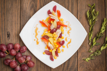 Salad with grapes and chicken on white dish. Wooden background. Top view
