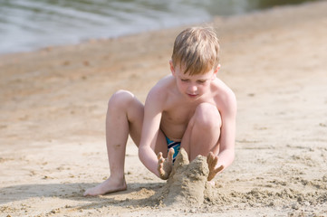 Little boy on the beach plays with sand