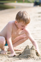 Little boy on the beach plays with sand