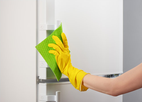 Hand in yellow glove cleaning white refrigerator with green rag