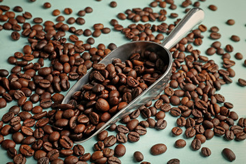 Roasted coffee beans and metal scoop on wooden table closeup