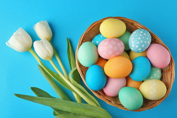 Basket with painted Easter eggs and flowers on blue background