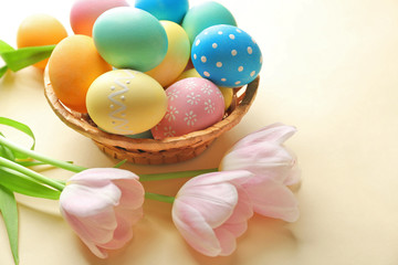 Basket with painted Easter eggs and flowers on beige background