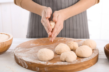 Woman making buns from raw dough on kitchen table