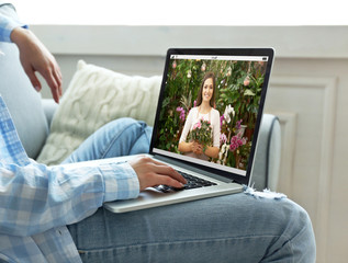 Fototapeta premium Video call and chat concept. Modern communication technology. Woman ordering flowers delivery online via laptop.