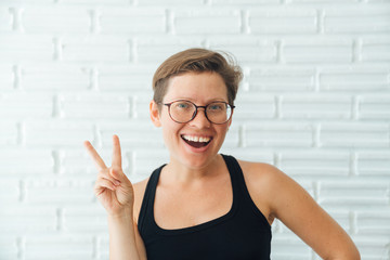Happy girl with glasses and short hair posing at the camera smiling and showing a gesture hippie...