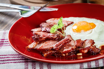 Slices of smoked bacon and fried egg on a red plate