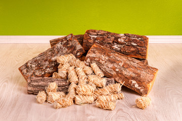 Stapel Feuerholz mit Anzündern auf hellem Parkett vor grünem Hintergrund