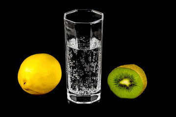 Naklejka na ściany i meble Kiwi, lemon and a glass of mineral water on black background close-up.