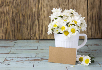 Blank brown paper tag and fresh daisies in white cup on wo