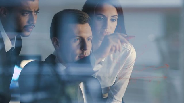 The three workers stand over the glass board and discuss graph