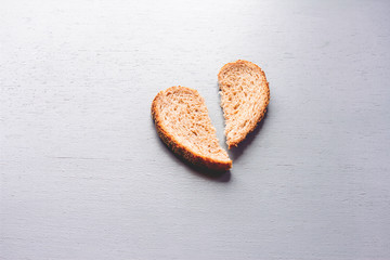 A shape of broken heart in the middle of rustic wooden table, shape of heart made from brown bread, heart breaking in to pieces