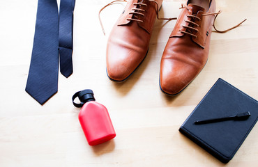 Fototapeta na wymiar A men accessories laying down on wooden table, black necktie, leather brown shoe, red perfume bottle,black electronic reader