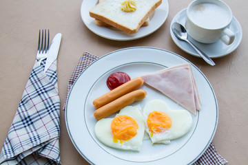 Breakfast with fried egg, ham, sausage, toast, butter, and coffee on table.