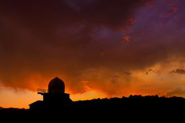 Fototapeta premium Weather observatory silhouette under a fiery sunset sky with orange clouds.