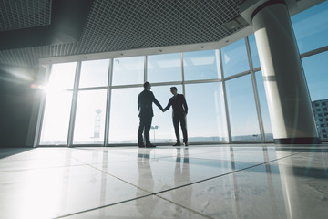 Full length side view of businessmen shaking hands in against panoramic windows