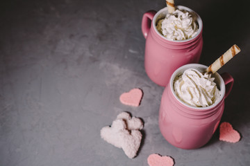 Two pink mugs with hot chocolate and cream on a gray concrete background. Drinks for a loving couple. The concept of Valentine's Day.