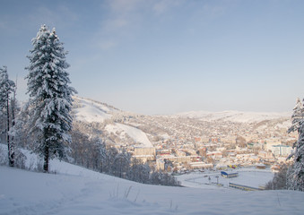 Winter snowy mountain ski slope and valley and village with frozen rime pine trees in the...