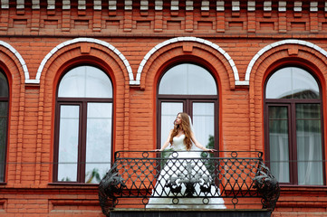Bride in wedding dress on balcony of luxury apartment at the red hotel building