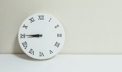 Closeup white clock for decorate show a quarter to nine or 8:45 a.m. on white wood desk and cream wallpaper textured background with copy space