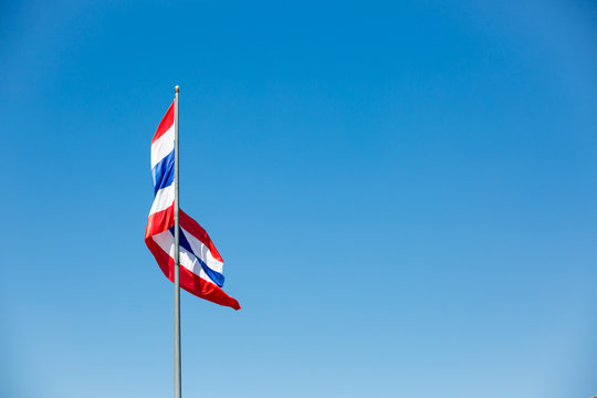 waving Thai flag of Thailand with blue sky background.