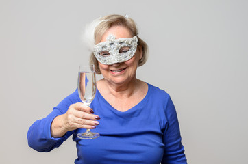 Smiling senior woman toasting with drink in mask