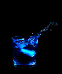 splash from ice cube in a glass of blue water or drink