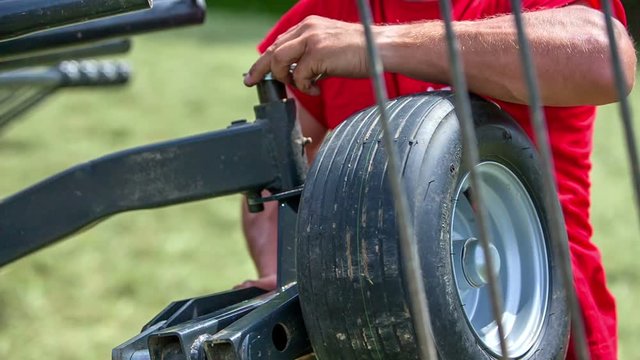 A young farmer is putting the wheel back on its place on the agricultural machinery. He is also putting a top on the side so that it fixedly connected.

