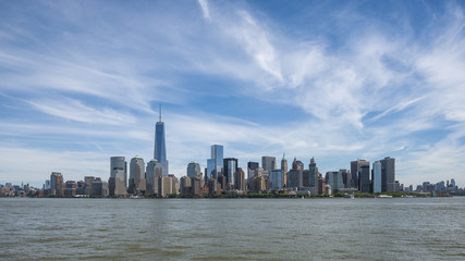 Fototapeta premium Vista dello skyline di Manhattan, NewYork da sud con il One Trade Center sulla sinistra e un cielo blu con qualche nuvola.
