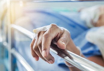 Close up hand of elderly patient with intravenous catheter for injection plug in hand during lying in the hospital bed