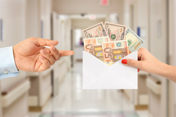 Woman bribing a man with an envelope full of money in a hospital hallway suggesting a corrupt...