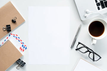 Blank a4 paper is in the middle of white office desk. Top view, flat lay.