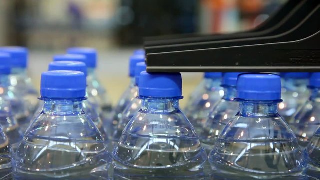 Many bottled water moves on conveyor belt at factory, close up view. Logo printed on the caps.