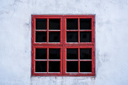 Old red weathered window with squares on white wall with worn texture.