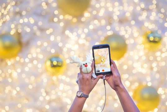 Woman's hand holding mobile phone and reindeer doll take a photo