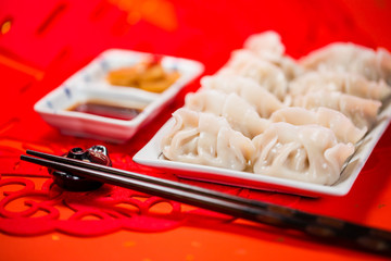 Chinese dumplings with sauce and paper-cut on red background. People will eat dumplings during Chinese New Year to pray for good fortune.