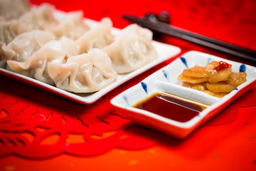Chinese dumplings with sauce and paper-cut on red background. People will eat dumplings during Chinese New Year to pray for good fortune.
