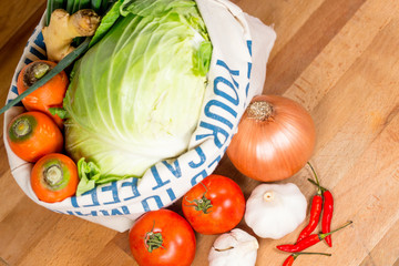 Fresh vegetables in weave bag holding, on wood on white background.