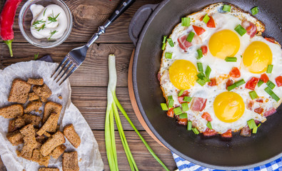 Fred eggs in pan with tomatoes and green fresh onion.