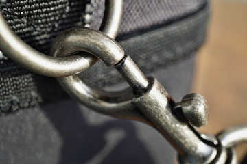 Macro detail of a snap-hook (snap-link) fastened to the black bag with silver loop as a symbol of safety link between two objects