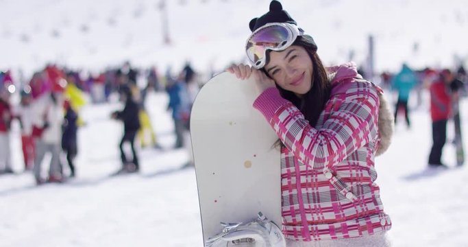 Side portrait of pretty young woman with snowboard relaxing on ski holiday. She waving her hand to camera.