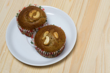 Banana cup cake with cashew nut on white dish and wood table.