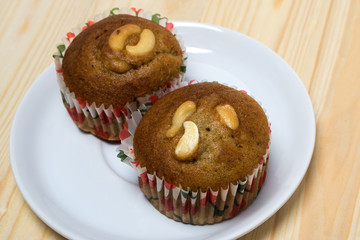 Banana cup cake with cashew nut on white dish and wood table.