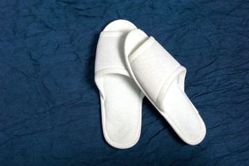 White cloth slippers on blue background in spa service.