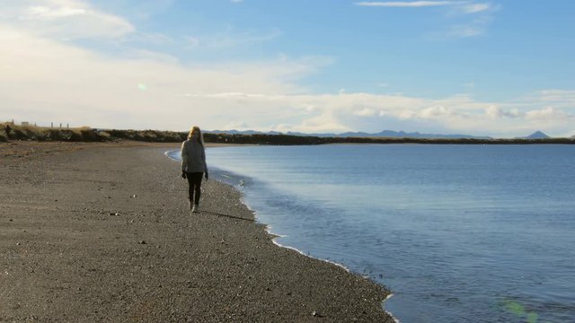 young tourist is walking on black volcanic beach in Reykjavik, smiling blond woman