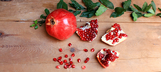 Ripe pomegranate fruit with a branch and leaves on a wooden table