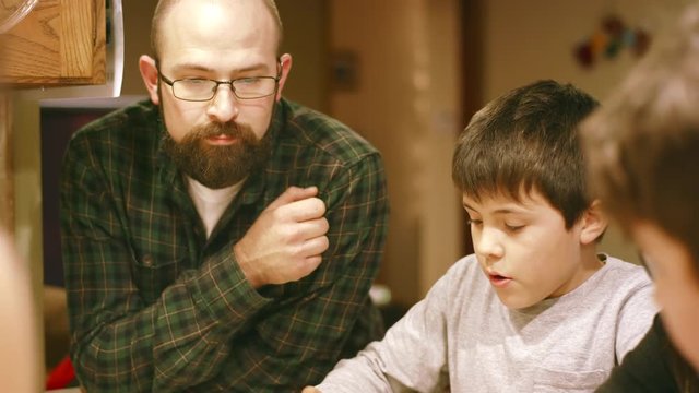 Family building a chocolate house together at dinner kitchen table, boy looking bored