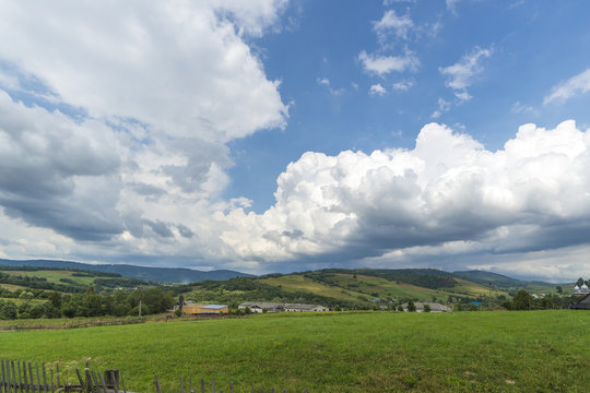 Mountain summer day landscape with clouds on blue sky, river and small houses. 